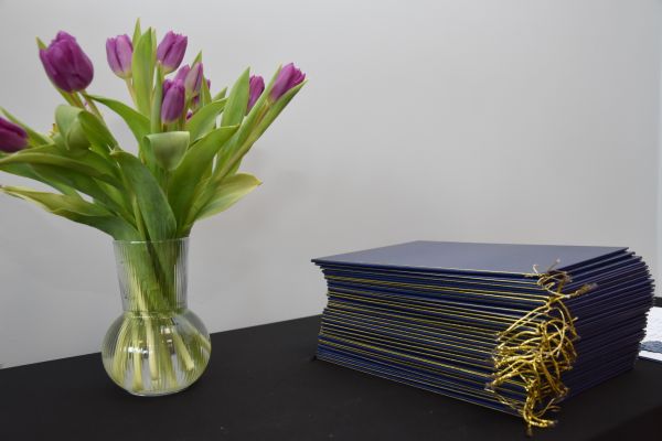 Na stoliku leżą certyfikaty dla specjalistów i stoi wazon z fioletowymi tulipanami