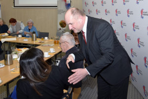 stojący mężczyzna poklepuje siedzącą kobietę po ramieniu