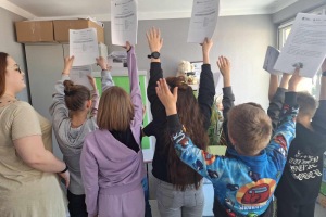 grupa dzieci podnosi w górę pliki kartek