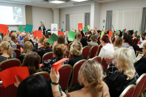 ludzie siedzą na krzesłach i trzymają w górze kartki