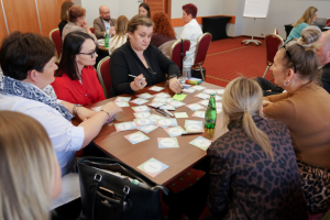 ludzie siedzą na krzesłach przy stole z rozsypanymi kartkami